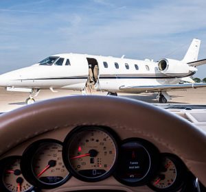 Private jet airplane on the airport track viewed from the seat of a car driver. Gauges and steering wheel are seen in front.