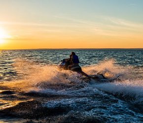People having fun riding a person watercraft/water scooter on the sea in the sunset.