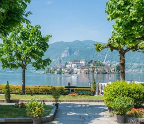 Orta with lake and island San Giulio in a sunny day with mountain and trees in Piedmont, Italy.